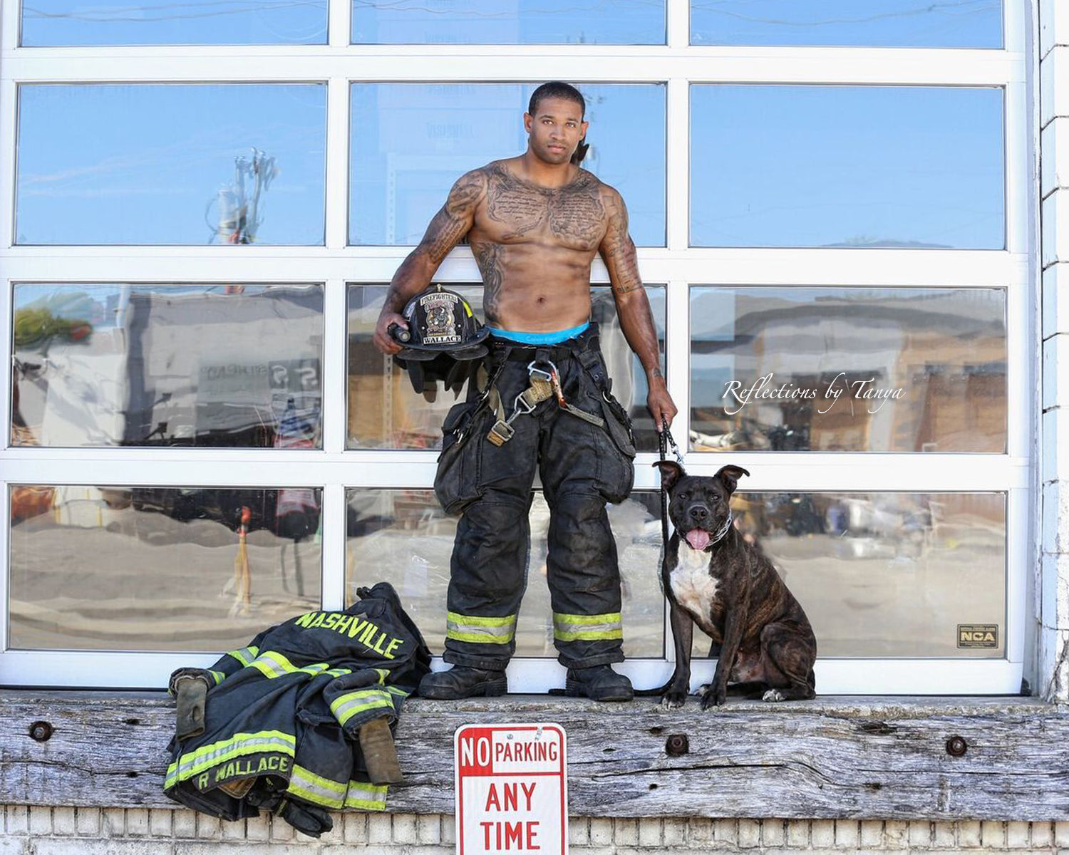 Man in firefighter gear with a dog in front of a building with large windows